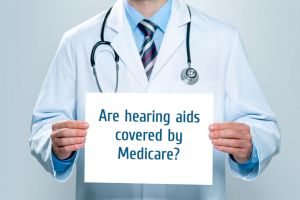 A doctor holds up a sign asking if hearing aids are covered by Medicare.