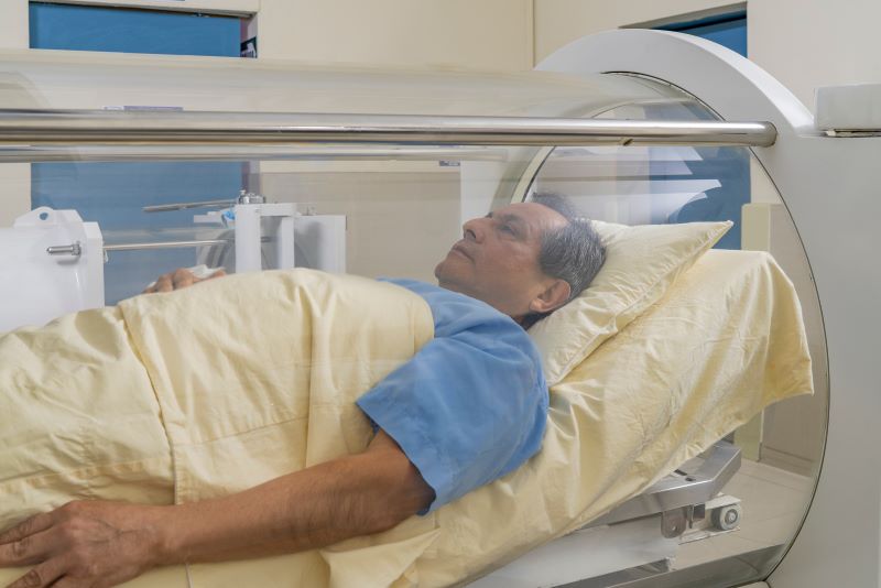 A man receives hyperbaric oxygen therapy in a hard-shell tank.