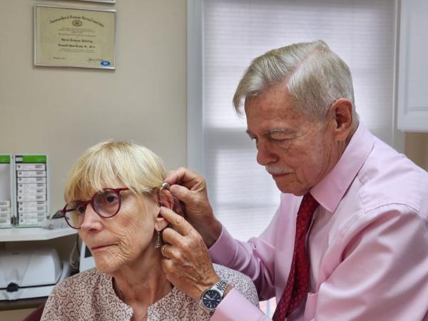 Dr. placing hearing aids in pt.'s ears